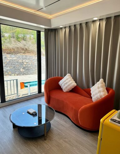 Heller Raum mit orangefarbenem Sofa, Kaffeetisch und großen Fenstern.